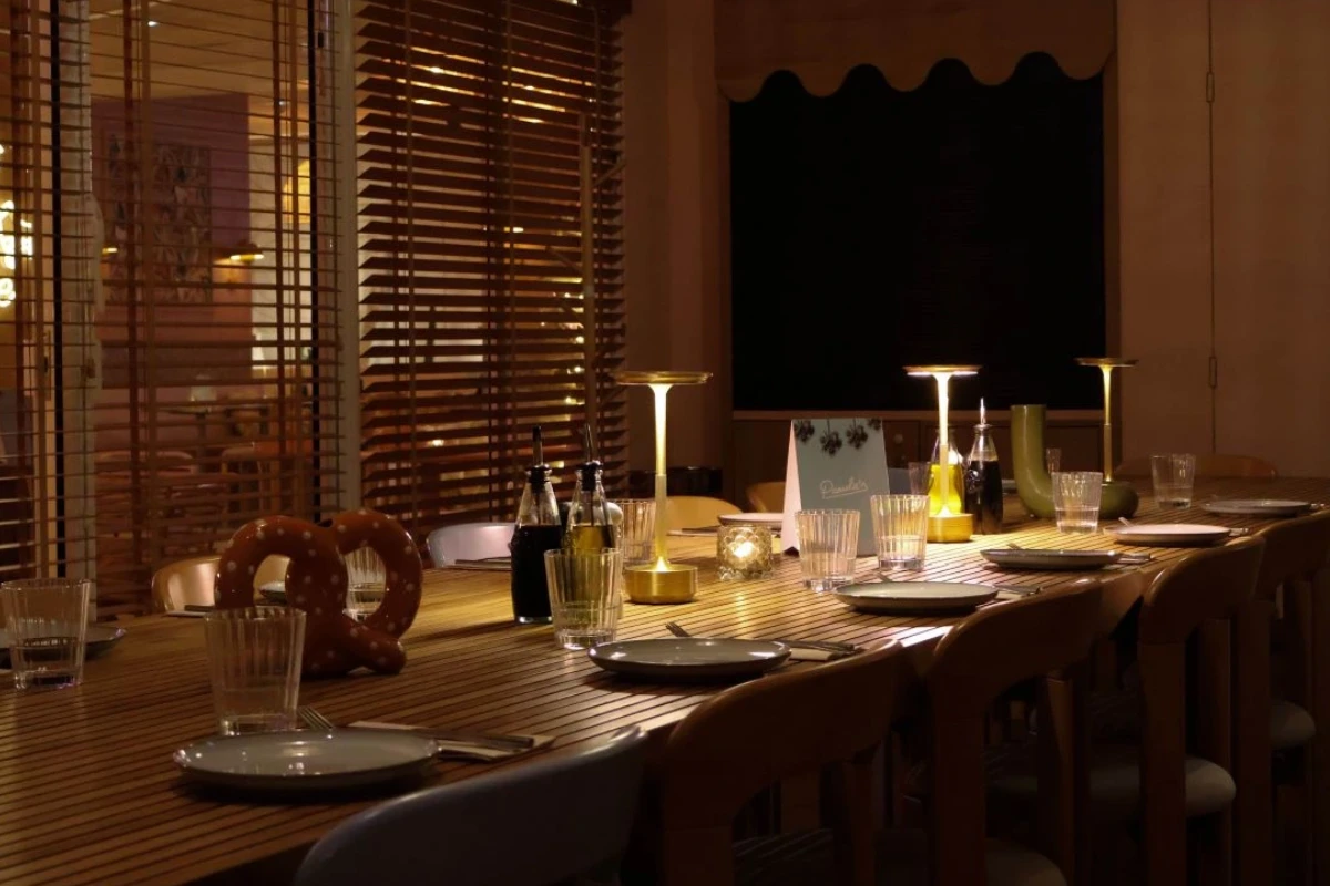 Long wooden banquet table set for a group event in the private dining room at Pamela's Bar in Nice, featuring dim lighting and wooden blinds.