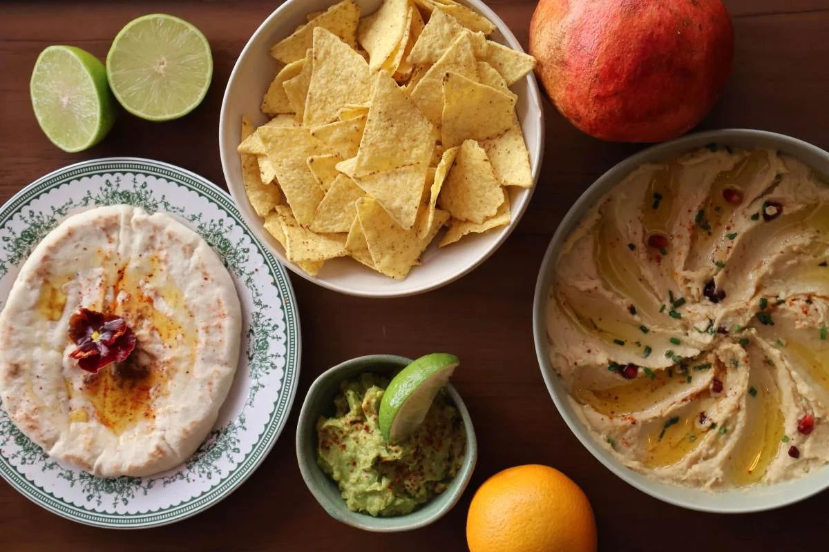 Top-down view of a homemade tapas platters featuring a large bowl of creamy hummus, fresh guacamole with lime, warm pita bread, and crunchy tortilla chips at Pamela's Bar in Nice.