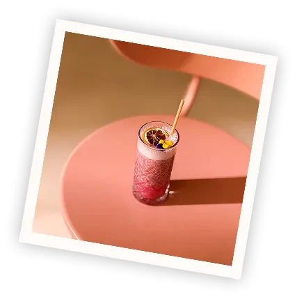 Polaroid-style photo of a pink raspberry cocktail garnished with a dried citrus slice, placed on a stylish pink chair at Pamela's Bar in Nice.