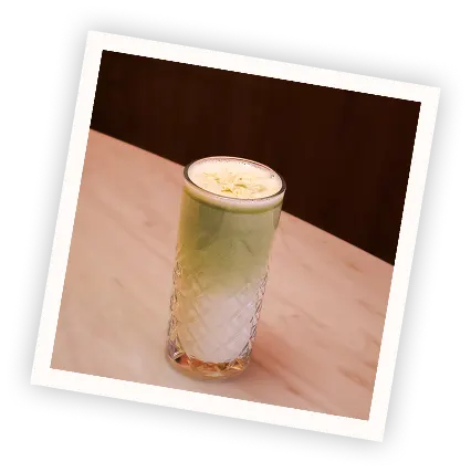 Polaroid-style photo of an iced matcha latte with a smooth foam layer in a faceted glass, placed on a wooden table at Pamela's Bar in Nice.