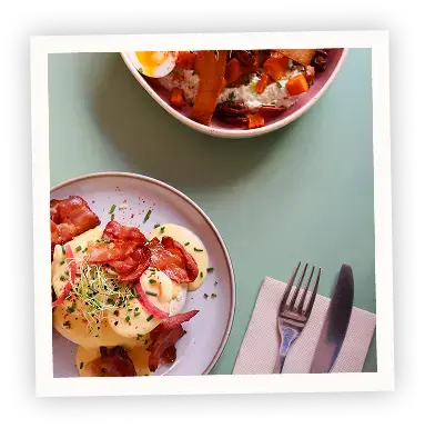 Polaroid-style photo of two brunch plates with crispy bacon Eggs Benedict and fresh herbs, served on a green table at Pamela's Bar in Nice.