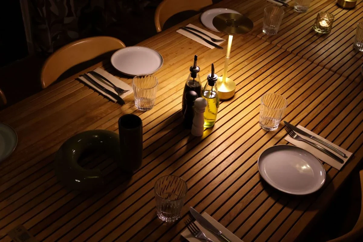Vue plongeante d'une grande table en bois dressée avec soin et éclairée par une lampe sans fil dorée dans la salle privative du Pamela's Bar à Nice.